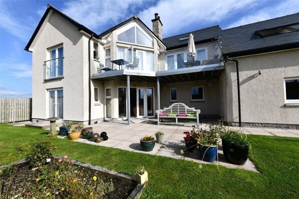 A two-story house with a balcony, a patio with outdoor furniture, and a garden area.