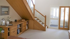 A room with a wooden staircase, a bookshelf, a desk, and a door leading to a balcony.