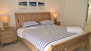 A wooden bed with a striped bedspread, two bedside tables with lamps, and a wall-mounted artwork.