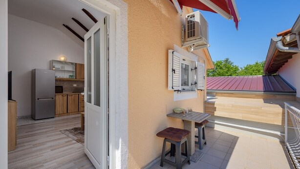Een moderne keuken met een koelkast en kasten, een eethoek met een tafel en stoelen, en een balkon met een rode luifel.