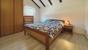 Een slaapkamer met een houten bed, een nachtkastje met een lamp, een kledingkast en een raam met gordijn.