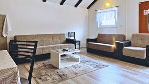 Een woonkamer met een bank, stoelen, een salontafel en een raam met gordijnen.