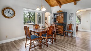 A dining area with a wooden table and chairs, a clock on the wall, and a fireplace with a glass door. - Three Wild Turkeys - Amazing Outdoor Spaces!  2 Decks! by Yosemite Region Resorts (Groveland)