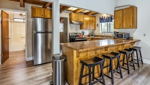A modern kitchen with wooden cabinets, a stainless steel refrigerator, a wooden island with bar stools, and a microwave. - Three Wild Turkeys - Amazing Outdoor Spaces!  2 Decks! by Yosemite Region Resorts (Groveland)