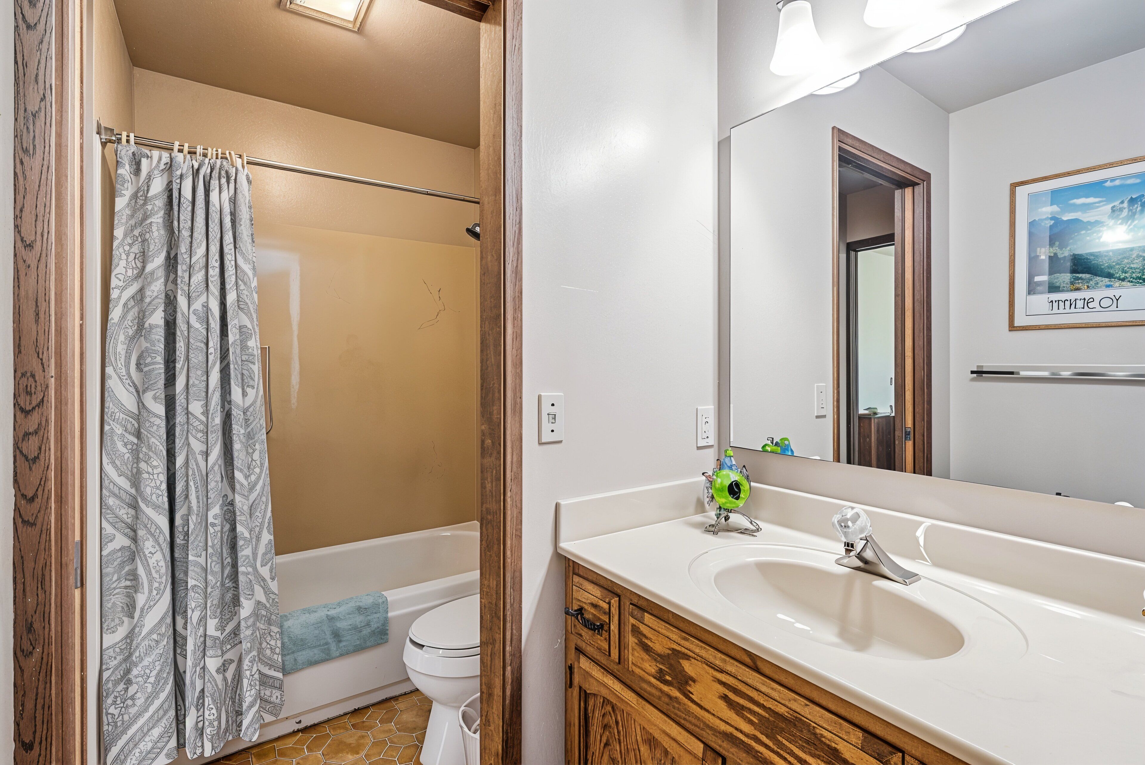 A bathroom with a shower, toilet, sink, and a mirror reflecting a door and a framed picture.