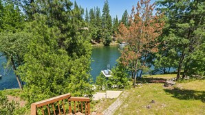 A wooden deck overlooking a lake with boats, surrounded by dense trees. - The Big Easy - Lakefront Only 1 mile to Popular Marina Beach! by Yosemite Region Resorts (Groveland)