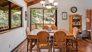 A dining area with a wooden table and chairs, a chandelier, and a bookshelf with books. - The Big Easy - Lakefront Only 1 mile to Popular Marina Beach! by Yosemite Region Resorts (Groveland)