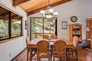 A dining area with a wooden table and chairs, a chandelier, and a bookshelf with books.