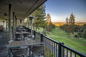 A covered outdoor seating area with tables and chairs, overlooking a well-manicured golf course.
