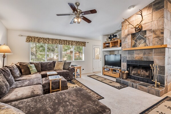 A living room with a sofa, TV, fireplace, and ceiling fan. - Star of the Mountain - The Star of Your Vacation by Yosemite Region Resorts (Groveland)