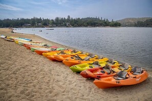 A row of colorful kayaks lined up on a sandy beach by a calm lake. - Star of the Mountain - The Star of Your Vacation by Yosemite Region Resorts (Groveland)