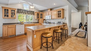 A spacious kitchen with wooden cabinets, a large island with stools, and a view of the outdoors. - Star of the Mountain - The Star of Your Vacation by Yosemite Region Resorts (Groveland)