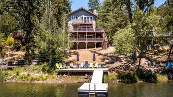 A two-story house with a dock extending into a lake, surrounded by trees.