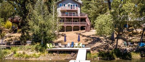 A two-story house with a dock extending into a lake, surrounded by trees.