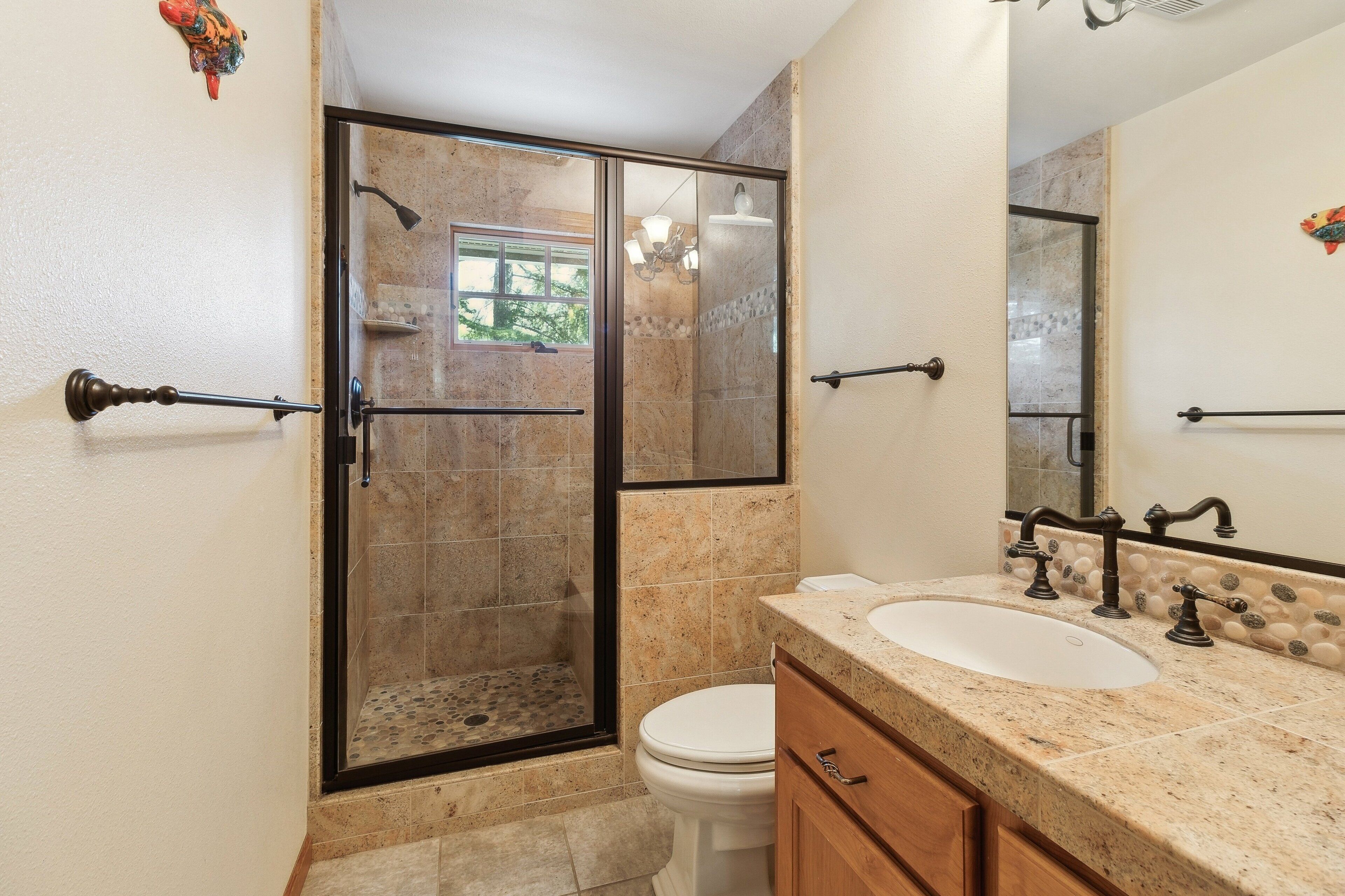 Een badkamer met een douche met glazen wand, een wit toilet, een wastafel met een marmeren blad en een spiegel met een decoratieve vis.