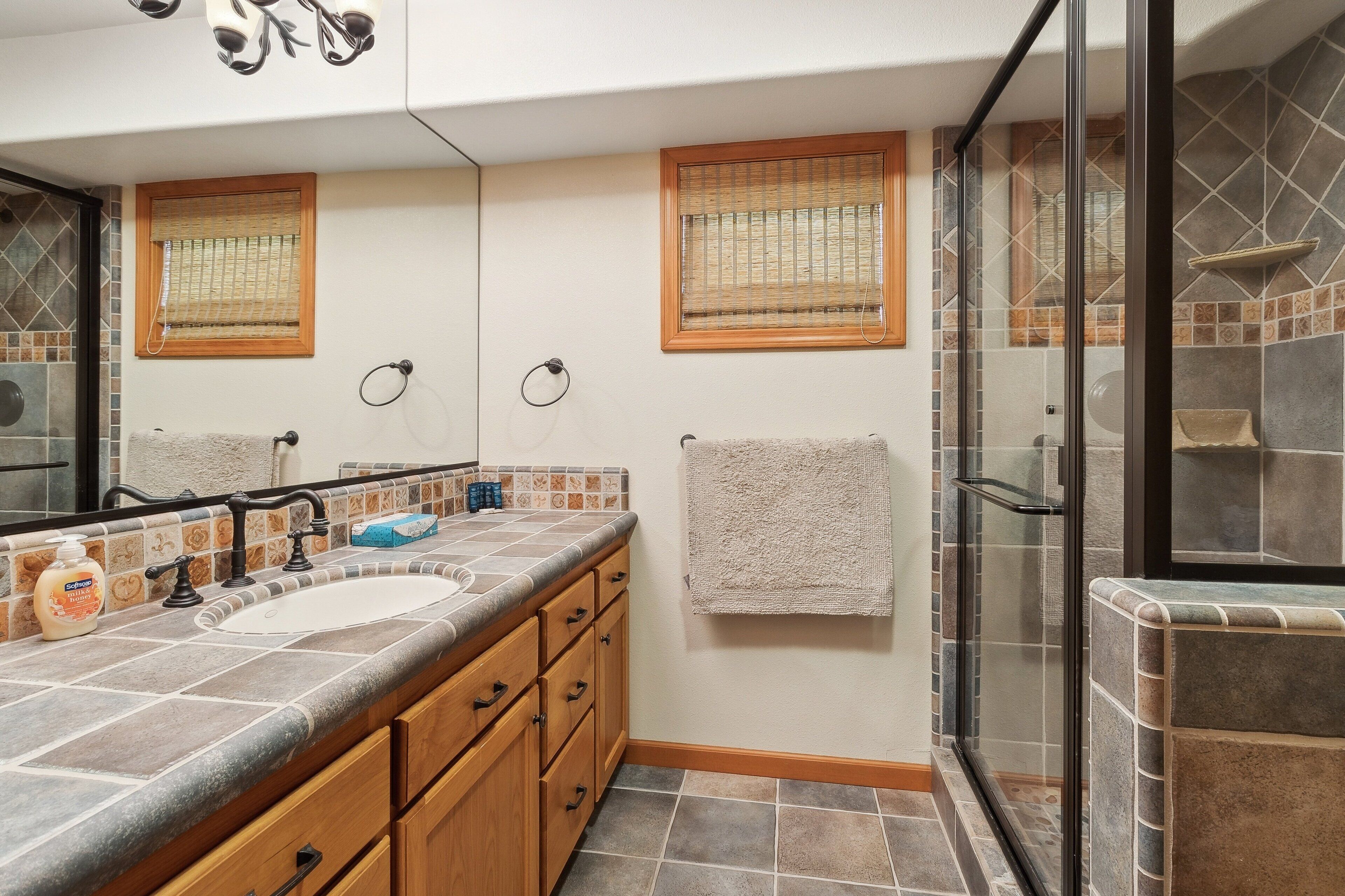 Une salle de bain avec deux lavabos, des meubles en bois, une cabine de douche en verre et des murs carrelés.