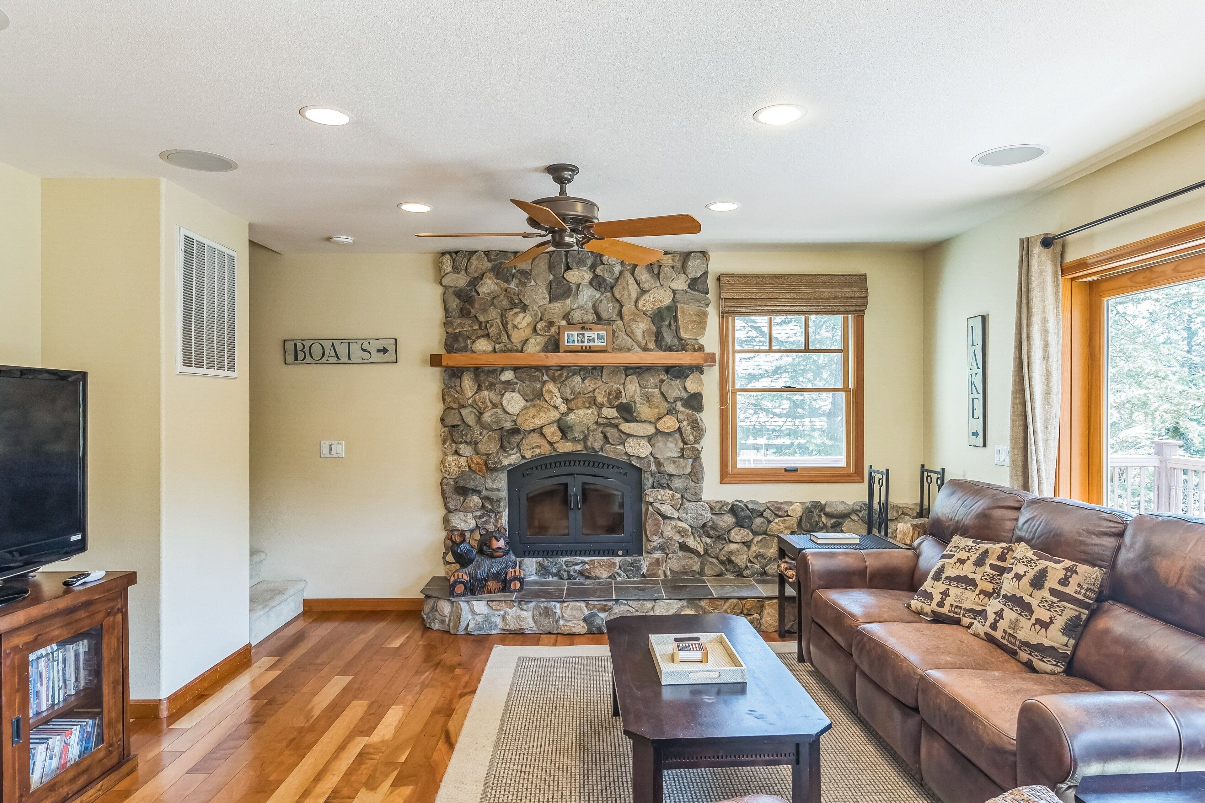 A living room with a stone fireplace, a leather sofa, a television, and a ceiling fan.