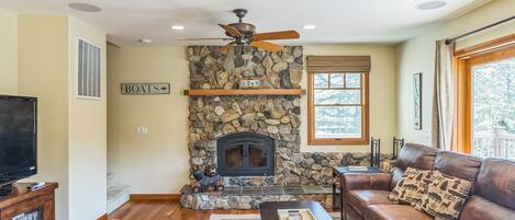 A living room with a stone fireplace, a leather sofa, a television, and a ceiling fan.
