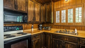 A kitchen with wooden cabinets, a stove, a microwave, a coffee maker, and a window with blinds. - The Hideout - Pet Friendly - The Perfect Spot for a Relaxing Yosemite Vacation by Yosemite Region Resorts (Groveland)