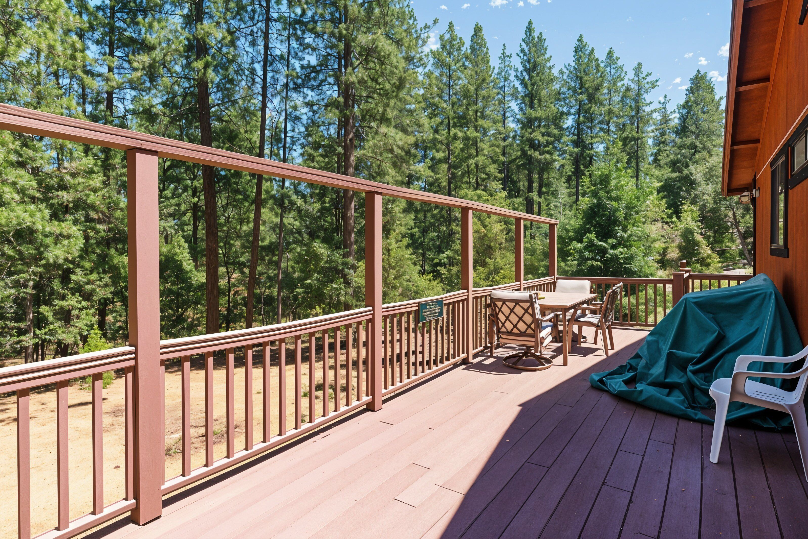 A wooden deck with a metal railing, a table with chairs, and a covered chair.