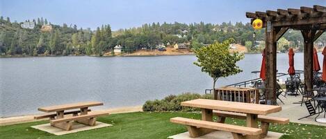 Un patio junto al lago con mesas de picnic y asientos al aire libre.