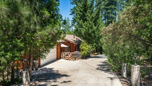 A wooden cabin with a covered porch, surrounded by tall pine trees and a clear sky. - The Hideout - Pet Friendly - The Perfect Spot for a Relaxing Yosemite Vacation by Yosemite Region Resorts (Groveland)