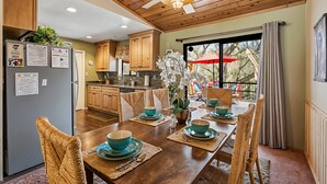 A dining area with a wooden table set for four, surrounded by wicker chairs. A ceiling fan is visible above the table. - Bigfoot Retreat - Close to Golf and the Beach by Yosemite Region Resorts (Groveland)