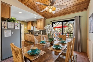 A dining area with a wooden table set for four, surrounded by wicker chairs. A ceiling fan is visible above the table.