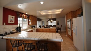 A kitchen with a central island, wooden cabinets, a refrigerator, and a dining area with chairs. - Yosemite Villa - Only 0.3 Miles from Lake Lodge Beach and Playground by Yosemite Region Resorts (Groveland)
