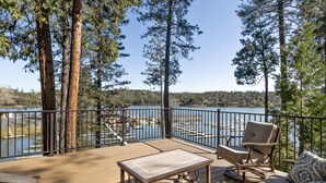 A deck with a table and chairs overlooking a lake with docks. - Dos Pinos - Spacious Lakefront Cabin w/ Game Room by Yosemite Region Resorts (Groveland)