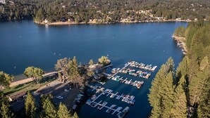 An aerial view of a marina with multiple docks and boats, surrounded by dense forest and a large body of water. - Dos Pinos - Spacious Lakefront Cabin w/ Game Room by Yosemite Region Resorts (Groveland)