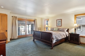 A bedroom with a large bed, a nightstand, a lamp, and a sliding glass door leading to a balcony. - Dos Pinos - Spacious Lakefront Cabin w/ Game Room by Yosemite Region Resorts (Groveland)
