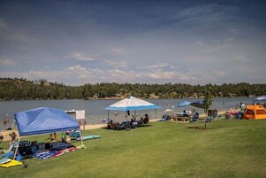 A lakeside camping area with tents, a covered seating area, and a grassy field.