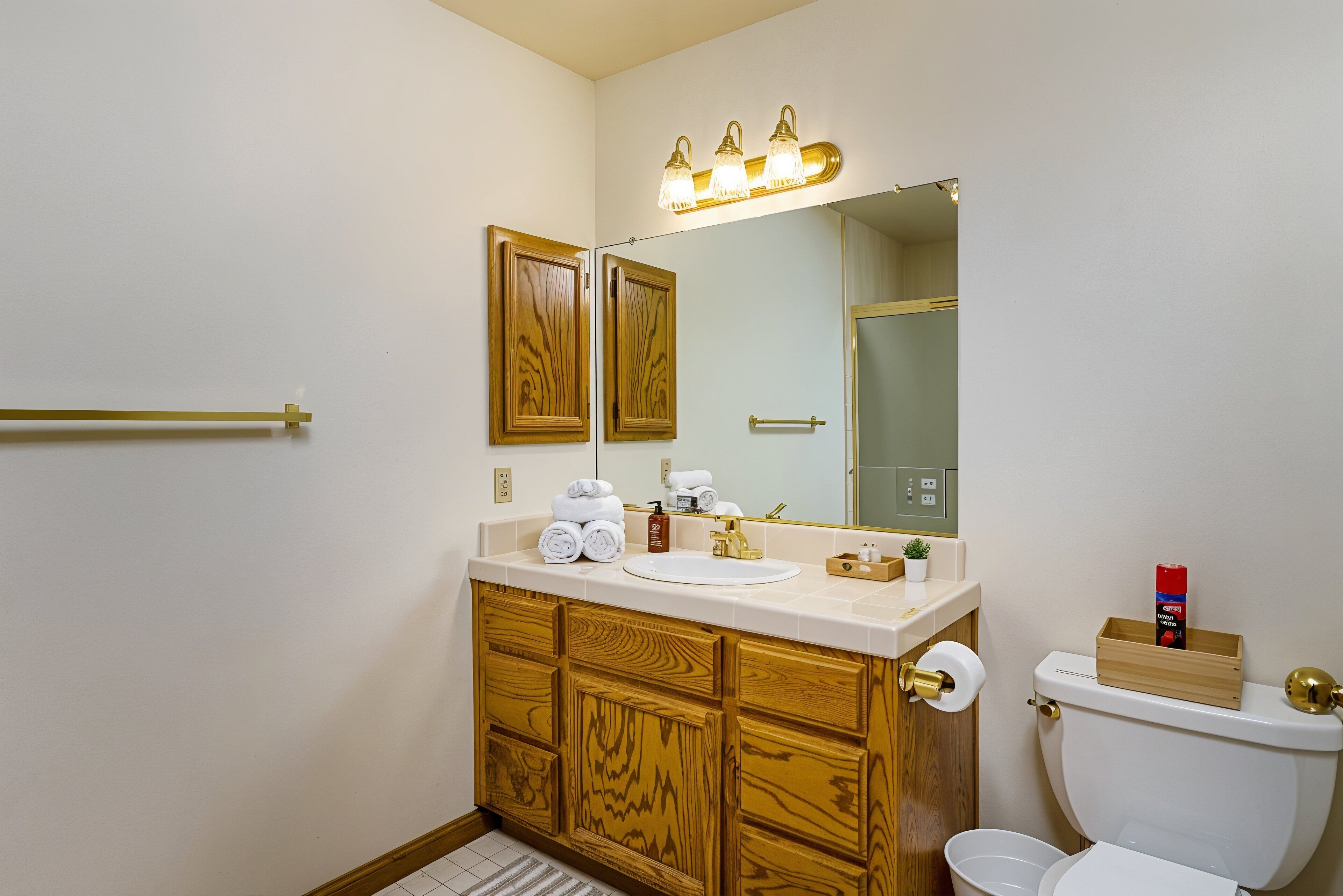 Une salle de bain avec des meubles en bois, un lavabo blanc, un miroir avec éclairage intégré et des toilettes.