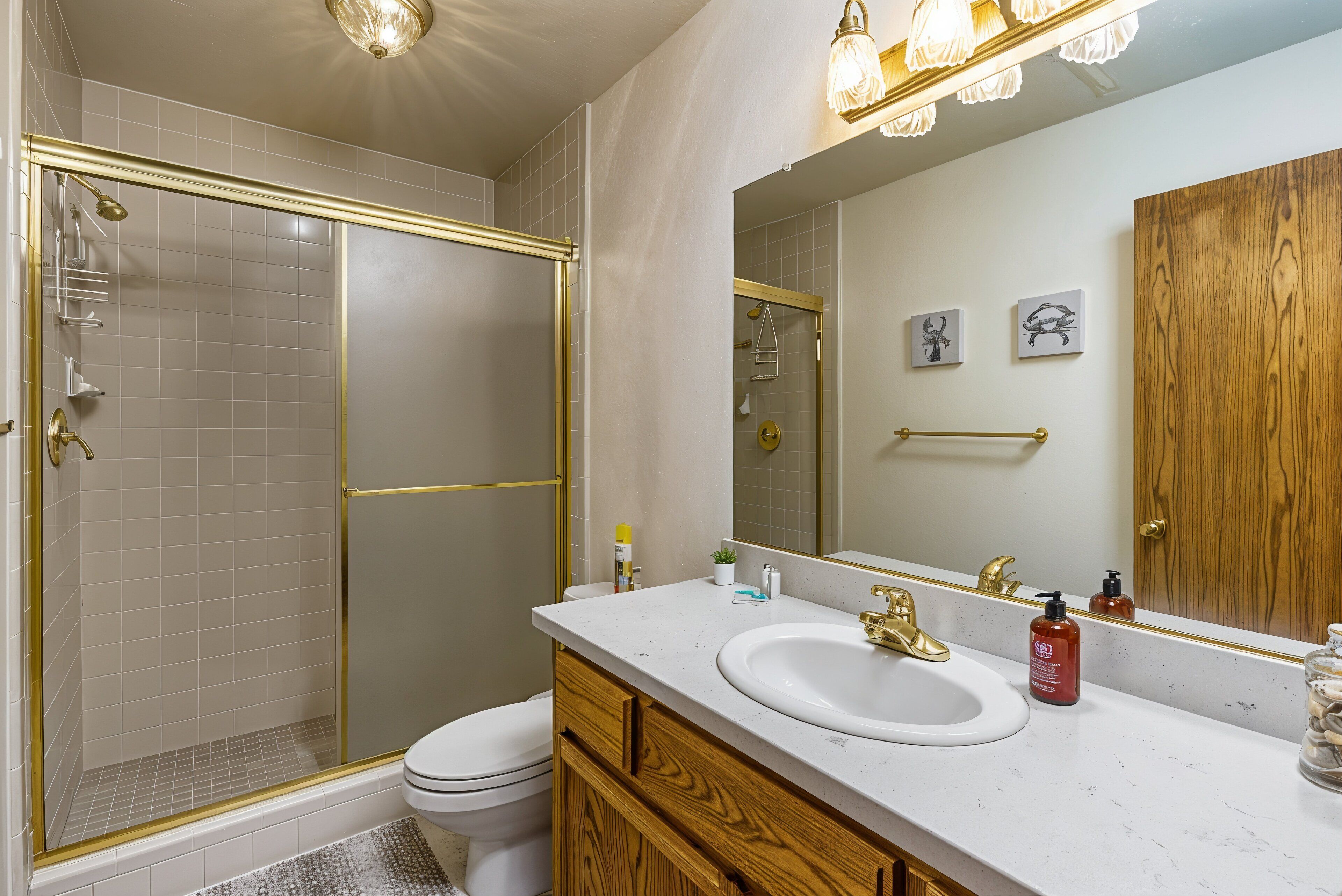 A bathroom with a shower, toilet, vanity with a sink, and a large mirror.
