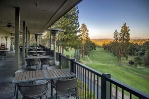 A covered outdoor seating area with tables and chairs, overlooking a well-manicured golf course.