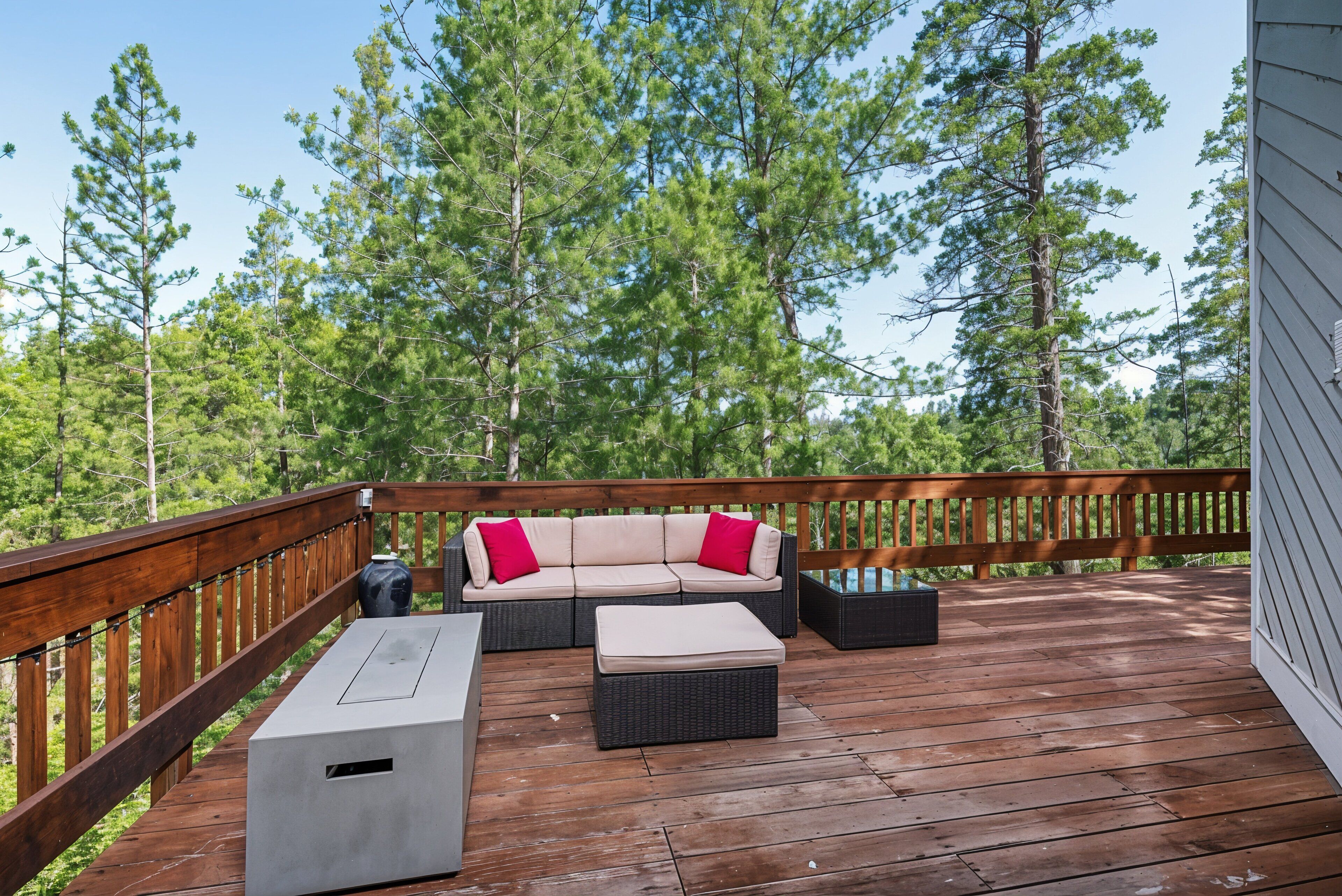 A wooden deck with a beige sectional sofa, two black ottomans, and a white table.