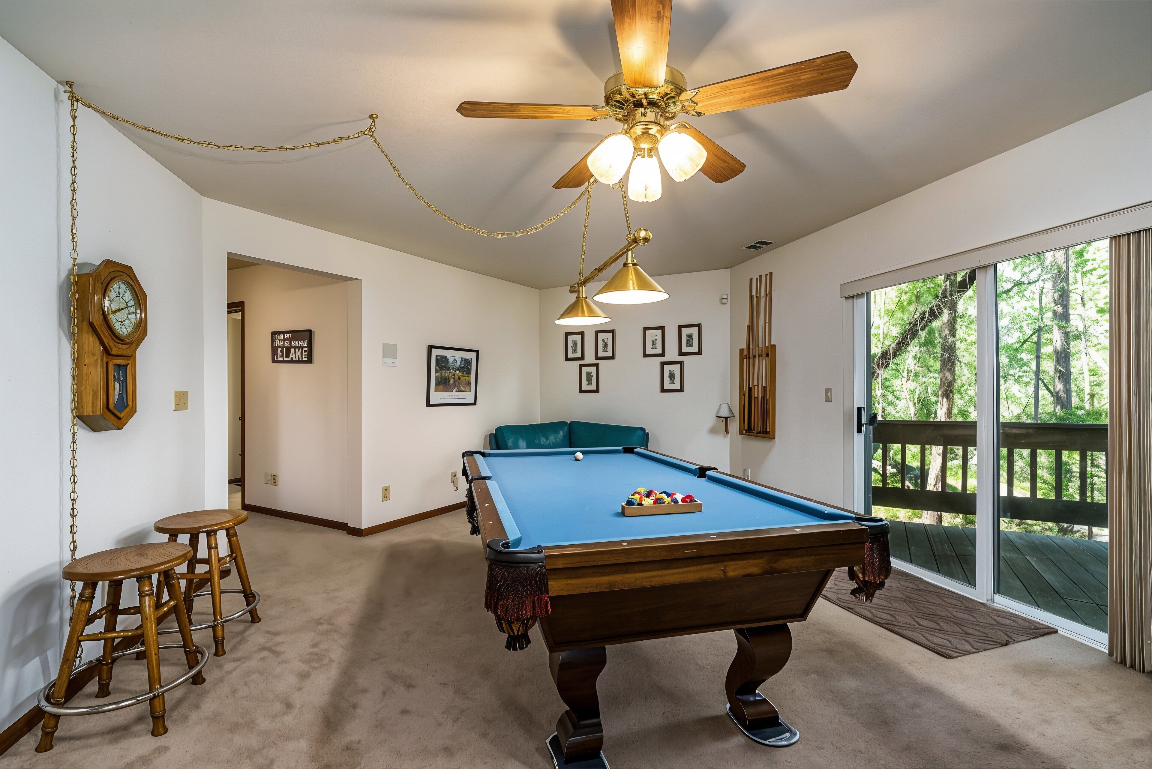 A pool table in a room with a ceiling fan, wooden stools, and a clock on the wall.