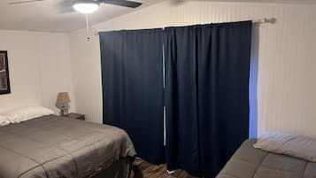 Een slaapkamer met twee bedden, een plafondventilator en een nachtkastje met een lamp.