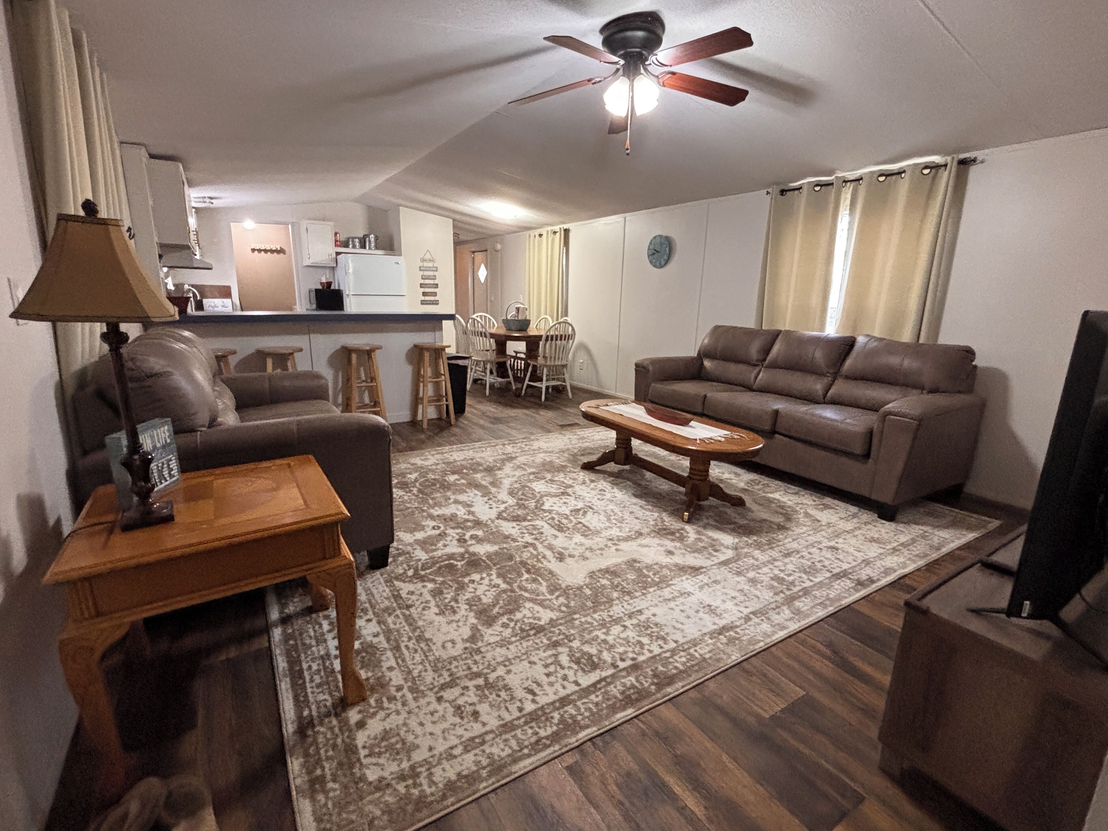 A living room with a brown leather sofa, a wooden coffee table, a lamp, and a television.