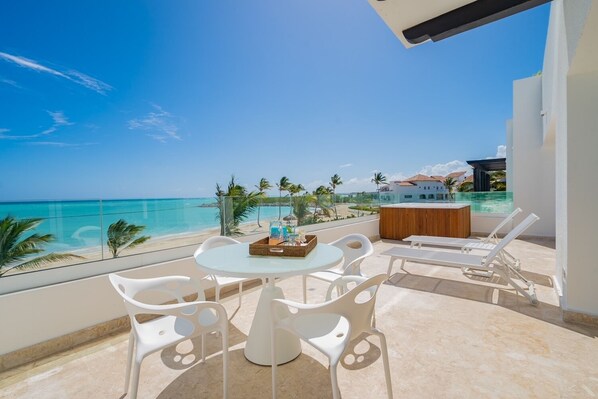 A balcony with a glass table, white chairs, and a view of the beach and ocean. - Stunning Beachfront Condo with Private Beach at Cap Cana (CAP CANA)