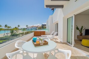 A balcony with a glass table, white chairs, a wooden bench, and a yellow ottoman. - Stunning Beachfront Condo with Private Beach at Cap Cana (CAP CANA)