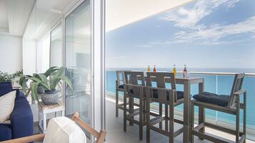 A balcony with a view of the sea, a table with chairs, and potted plants.