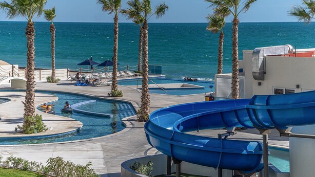 A resort pool area with multiple water slides, palm trees, and a view of the ocean. - *Stunning* 2BR condo at Encantame Towers Velero 2302 in playa Encanto (Puerto Peñasco)