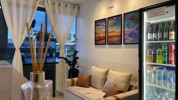 A modern living room with a sofa, a decorative plant, and a beverage refrigerator stocked with various drinks. - Pousada Mar de Luna (Penha)