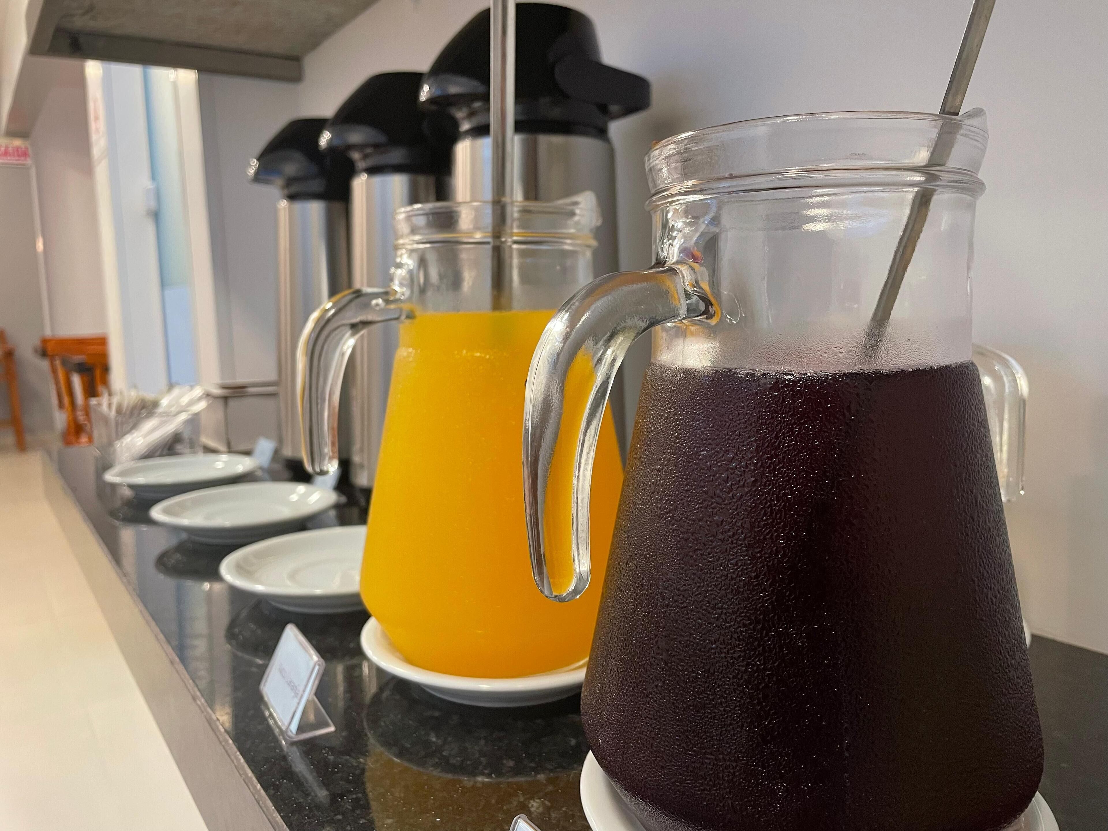 Una estación de bebidas con una jarra de té helado y una jarra de jugo de naranja.