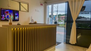 A reception area with a TV, a sign reading "SAÍDA," and a view of the street outside. - Pousada Mar de Luna (Penha)