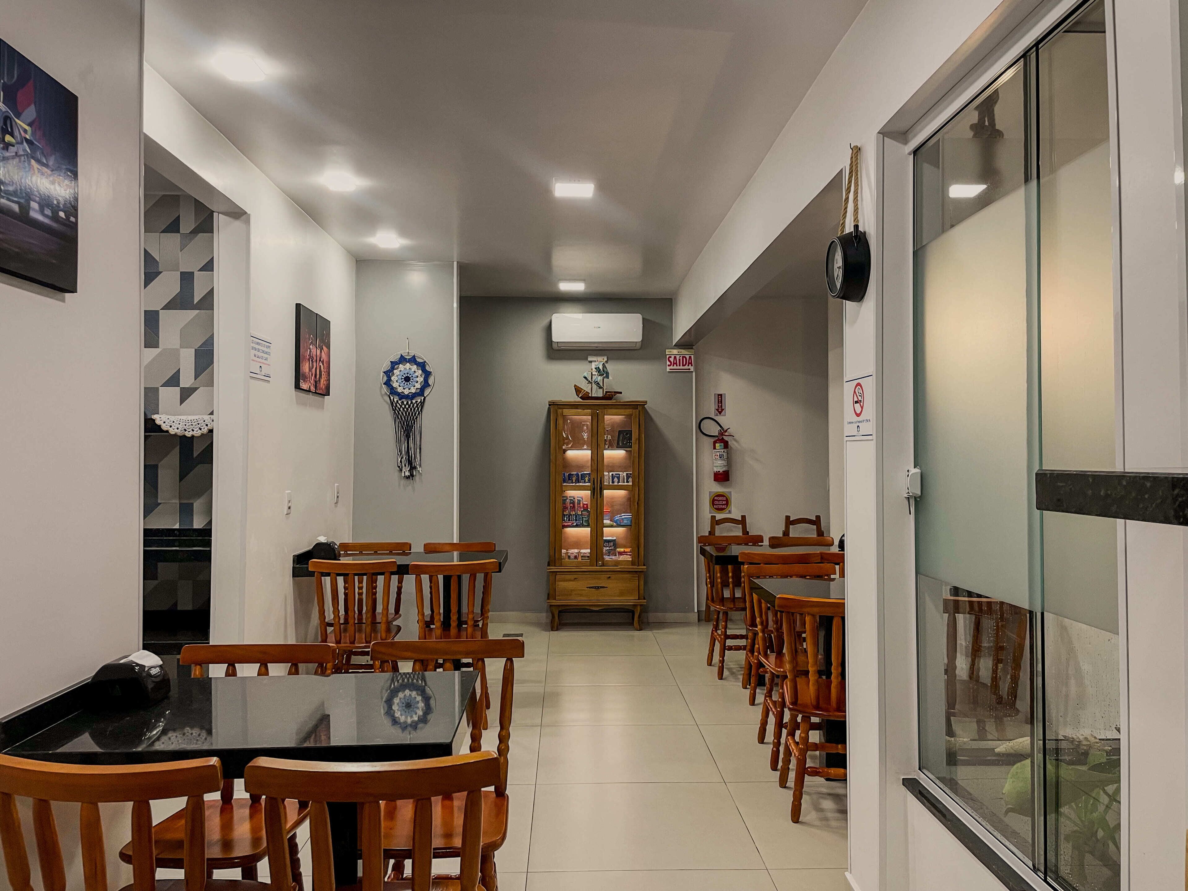 A hallway with a dining area featuring wooden chairs and a glass-top table, a cabinet with books, and a dreamcatcher on the wall.