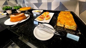 A buffet with various dishes including a cake, Bruschetta, and Torta de frios. - Pousada Mar de Luna (Penha)