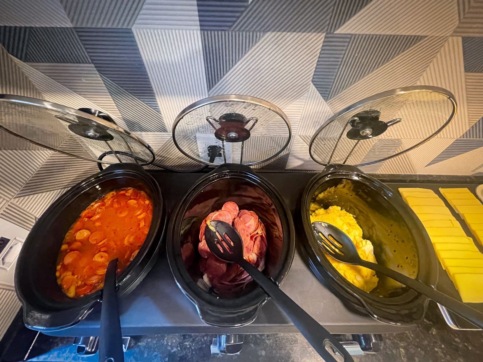 Three food dispensers with different dishes: a tomato-based soup, a meat dish, and scrambled eggs.